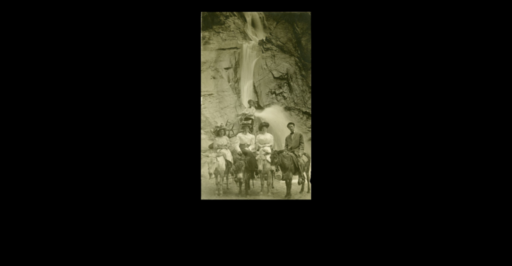 Sepia photograph of the Bernstein family, all wearing early-1900s style clothing and riding donkeys, posed in front of Seven Falls waterfall