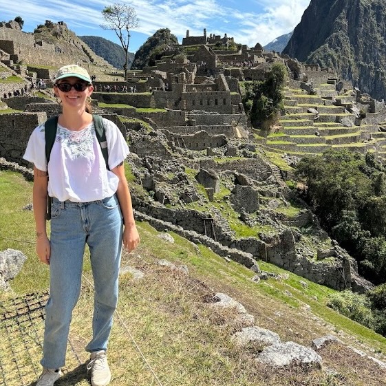 A woman stands in front of historical ruins.