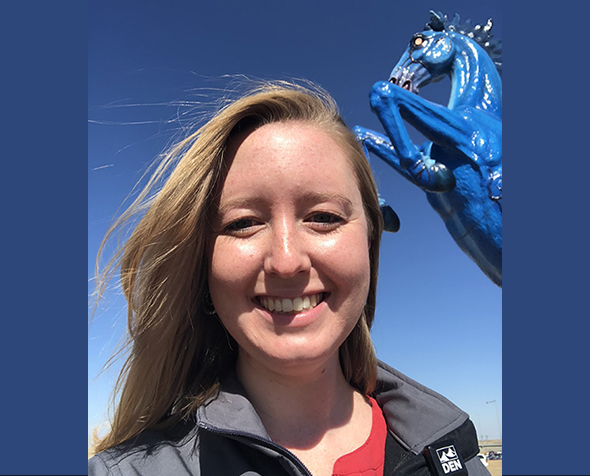 Emily Williams stands in front of the blue stallion statue at the entrance of Denver International Airport