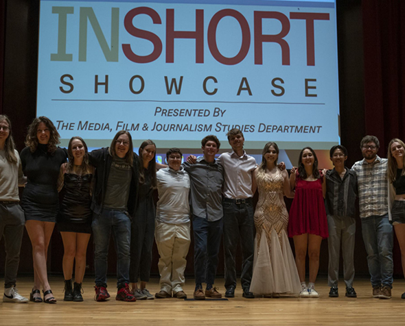 12 students stand next to each other in a line onstage in front of a projector that reads "InShort Showcase"