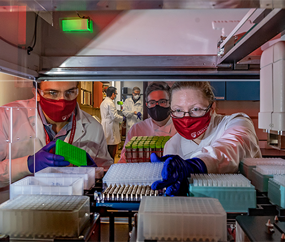 three people peering over covid 19 spit lab samples 