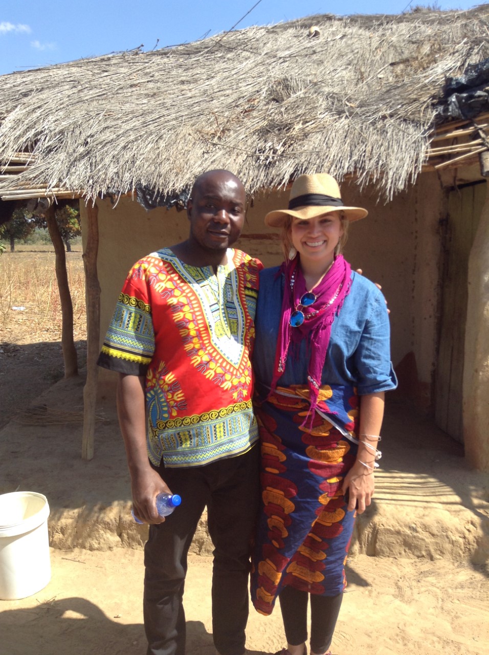Elton Chimwemwe Chavura (left) and Ivey Bostrom (MA '18) stand in front of a building with a thatched roof in Malawi