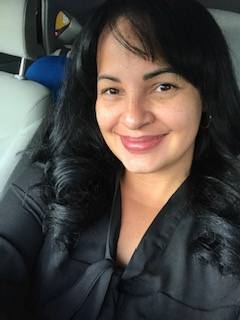 A woman with dark hair and a leather jacket sits in a car. 
