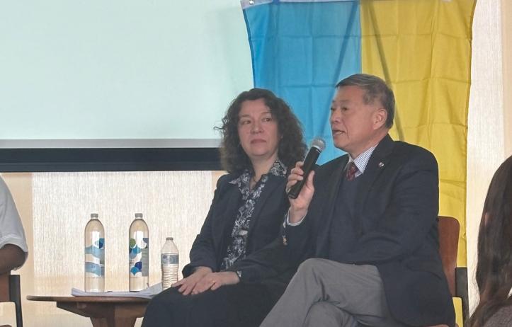 Dr. Nadia Kaneva and Dr. Suisheng Zhao sit in front of a Ukraine flag