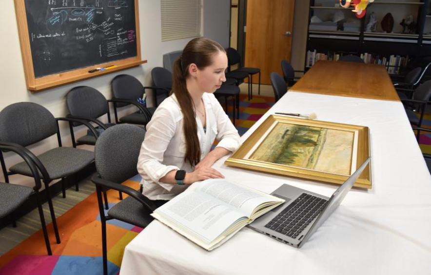 Woman looking at a painting with a laptop and a notebook for research