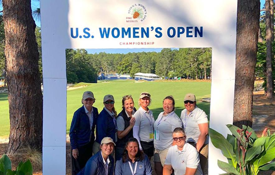 Turfgrass team poses in a cutout that says "U.S. Women's Open" in front of the golf course.