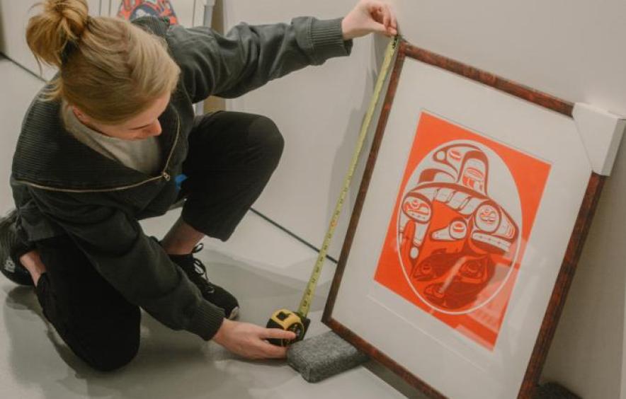 Art student measures a framed 2D artwork during a hanging workshop