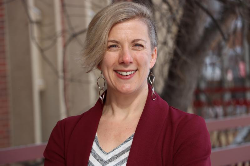 A woman smiles at the camera while standing outside.