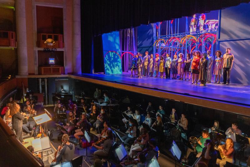 Wide photo of the stage and orchestra pit during the performance of an opera at the Newman Center.