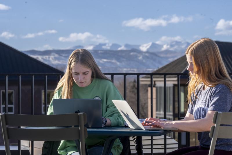 Two female students working on their laptops outdoors on the roof of the Community Commons.