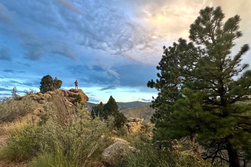 A landscape shot of a person standing on a large rock formation against a beautiful blue sky.