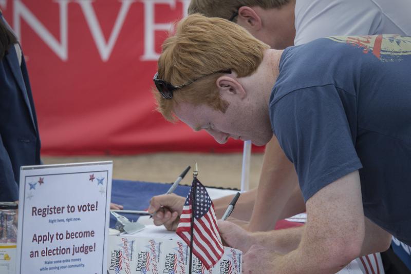 A young man registers to vote at a table with an american flag on it.