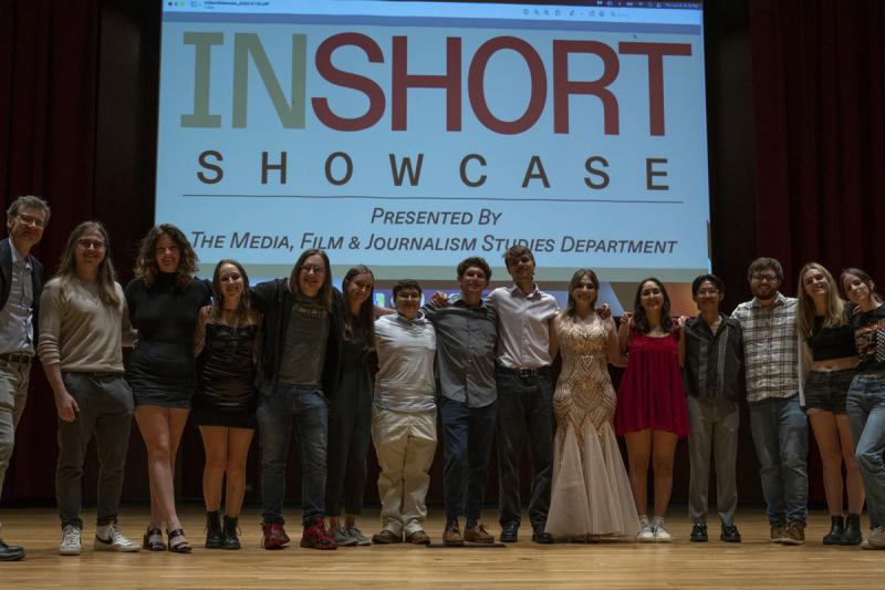 12 students stand next to each other in a line onstage in front of a projector that reads "InShort Showcase"