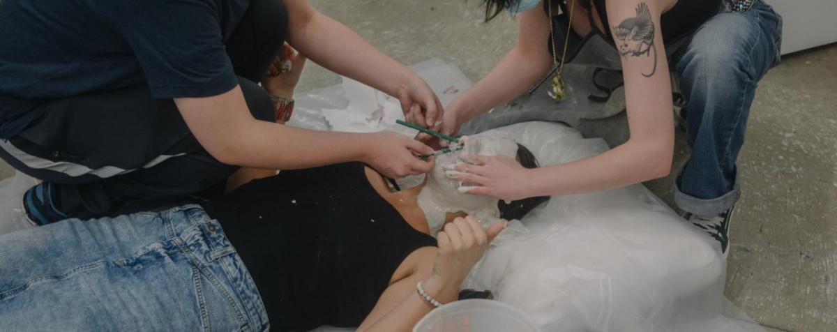 Students apply rubber to another's face to create a mold