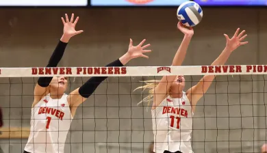 Two female volleyball players block at the net.