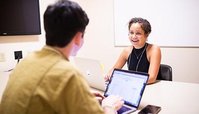 Two students talk over their laptops in a study room