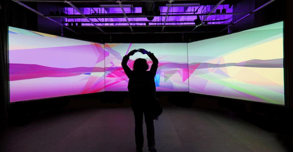 A person standing in front of two giant screens in The Hypercube, an EDP program space on DU's campus