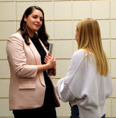 Two women stand in a hallway talking.