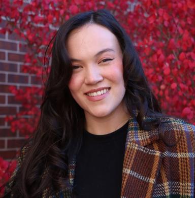 A person smiles at the camera in front of a tree.