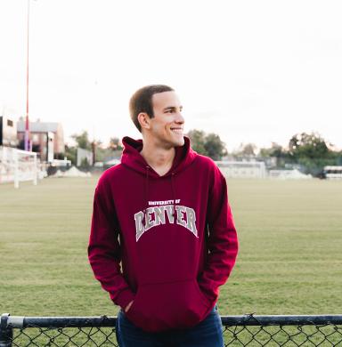 A man stands in front of an sports field smiling.