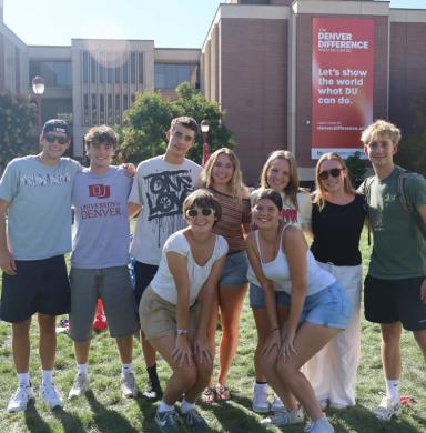 Students group together and smile in front of Sturm hall on the DU campus.