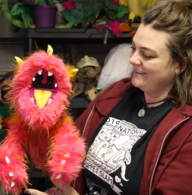 A woman holds a puppet and is smiling at it.