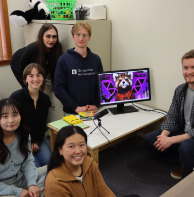 Students sit around a computer smiling.