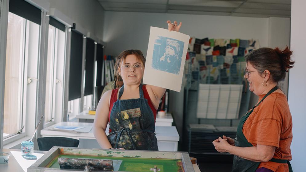 woman holding screen print up to camera as another looks on