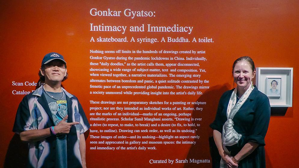 man and woman standing in front of wall with art exhibition description