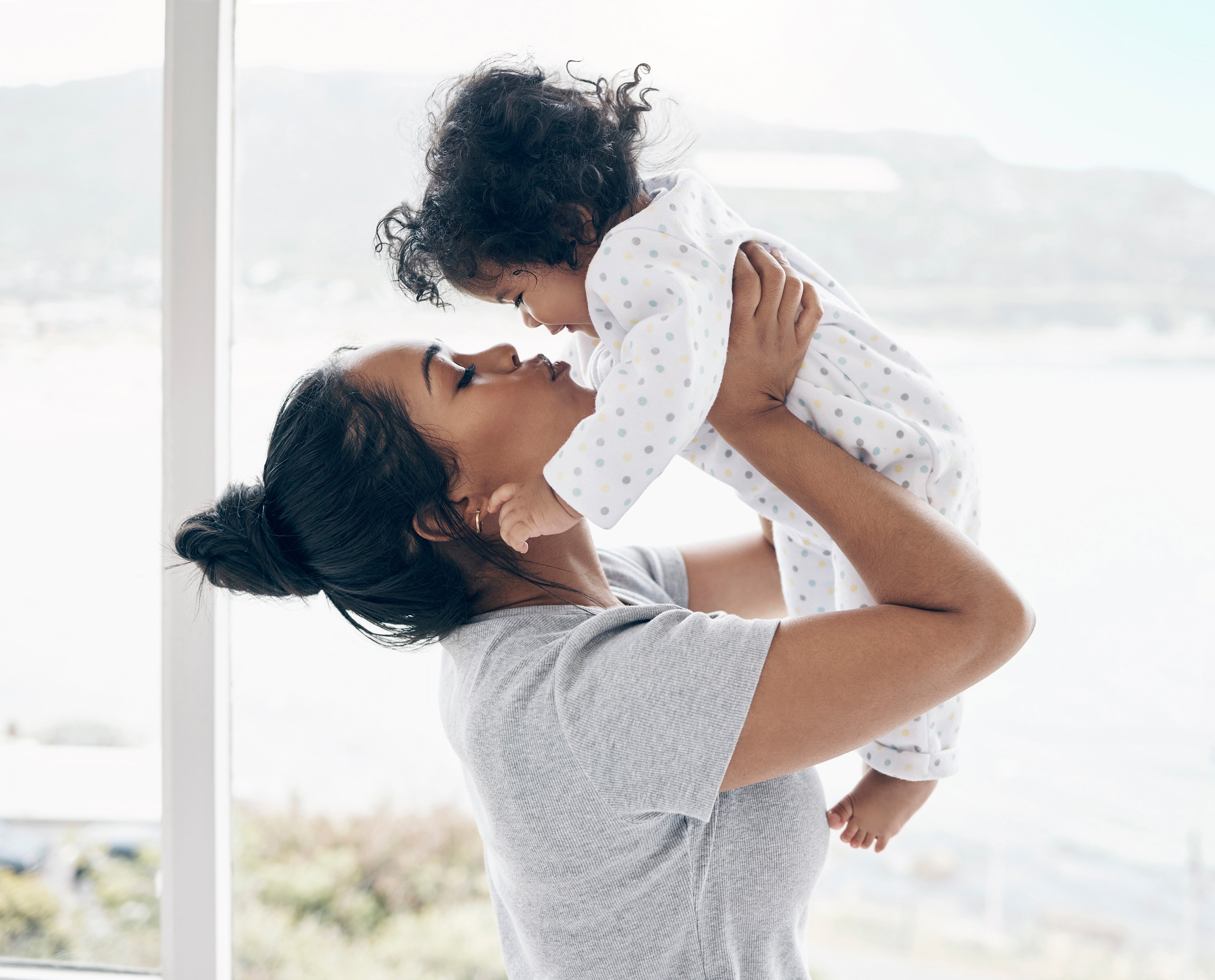 A young mother holds an infant up to her face and kisses them.