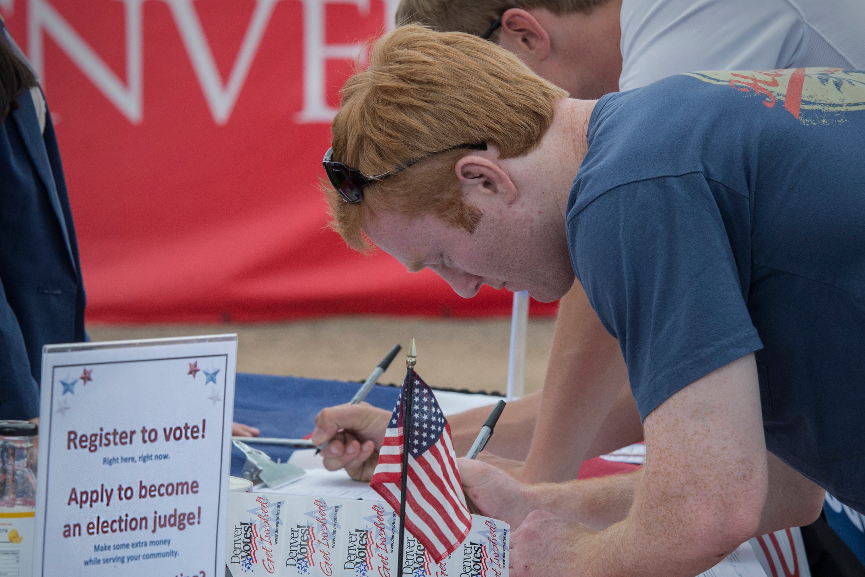 A young man registers to vote at a table with an american flag on it.